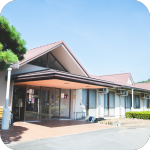 平屋造りの介護施設の外観。白壁とブラウンの屋根が特徴的です。