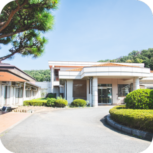 施設の玄関・車寄せ。モダンな平屋建築で、駐車スペースと植栽が整備されている。
